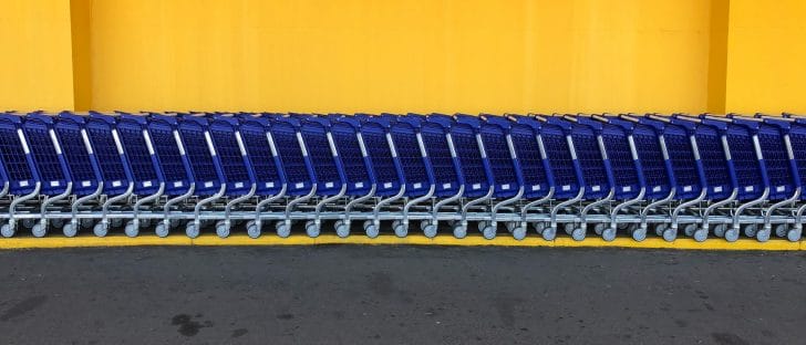 A line of blue shopping supermarket carts stand against the yellow wall