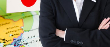 A woman in professional attire stands before a backdrop of the Japanese map and flag, symbolizing women's empowerment in Japanese business.